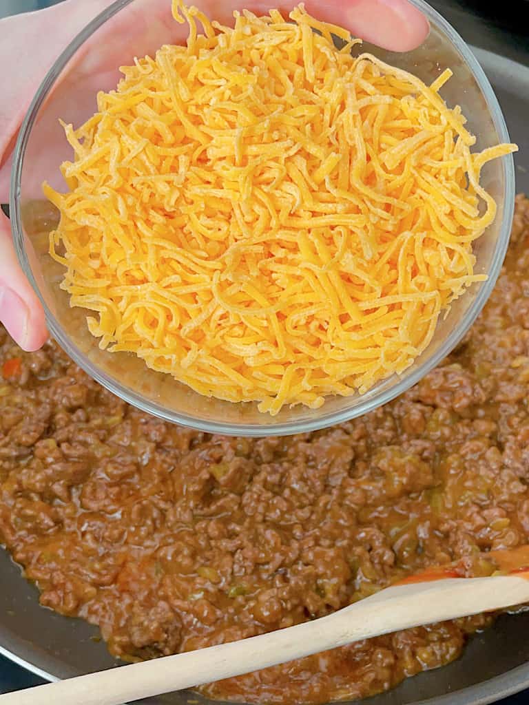 Shredded cheddar cheese in a bowl over a pan of ground beef.