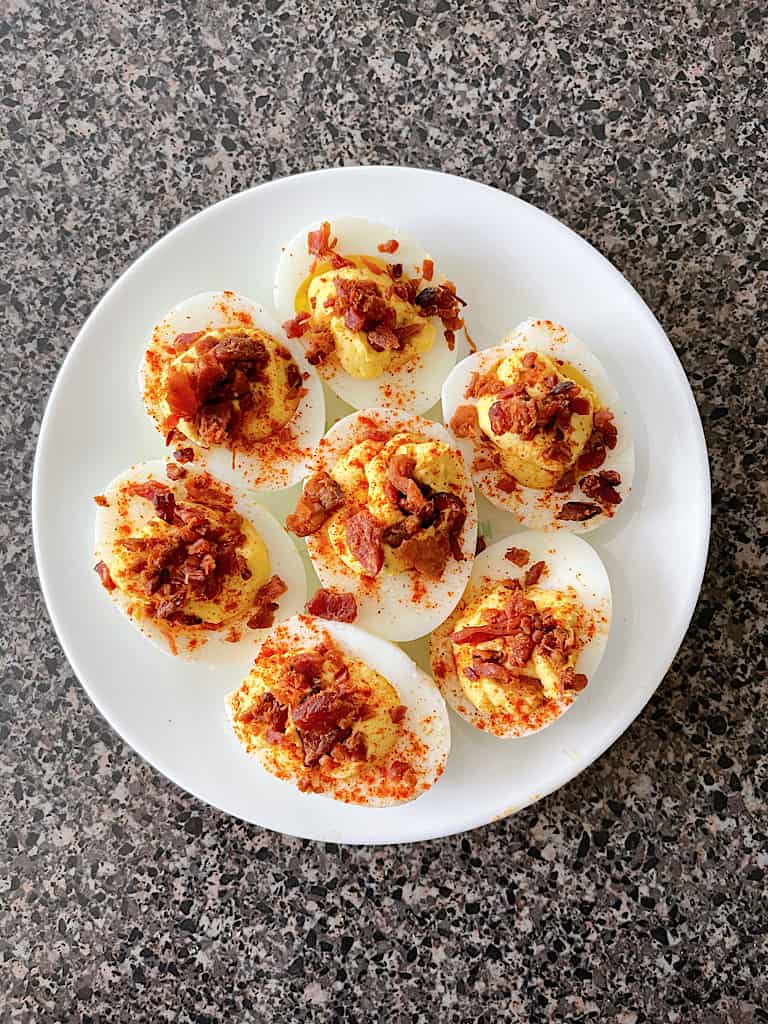 A plate of deviled eggs topped with bacon.