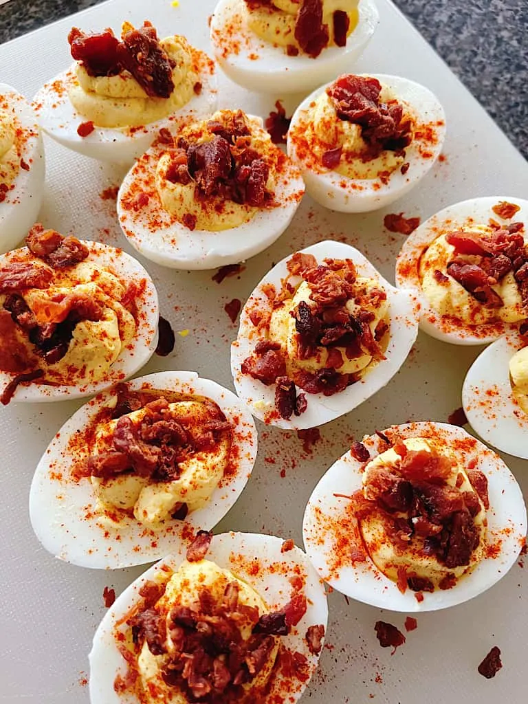 A plate of deviled eggs topped with bacon pieces.