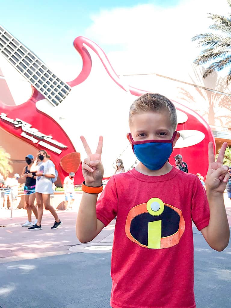 A boy holding up four fingers in front of Rock 'n Roller Coaster at Disney's Hollywood Studios at Disney World in Florida.