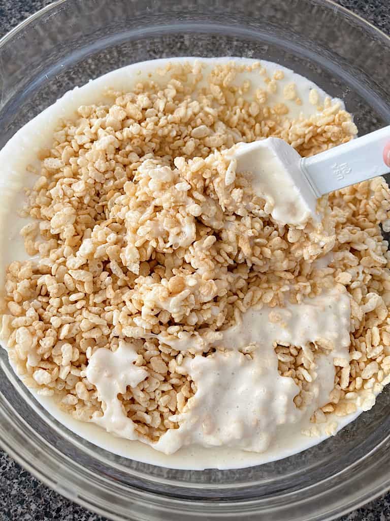A spoon mixing together melted marshmallows and Rice Krispies cereal.