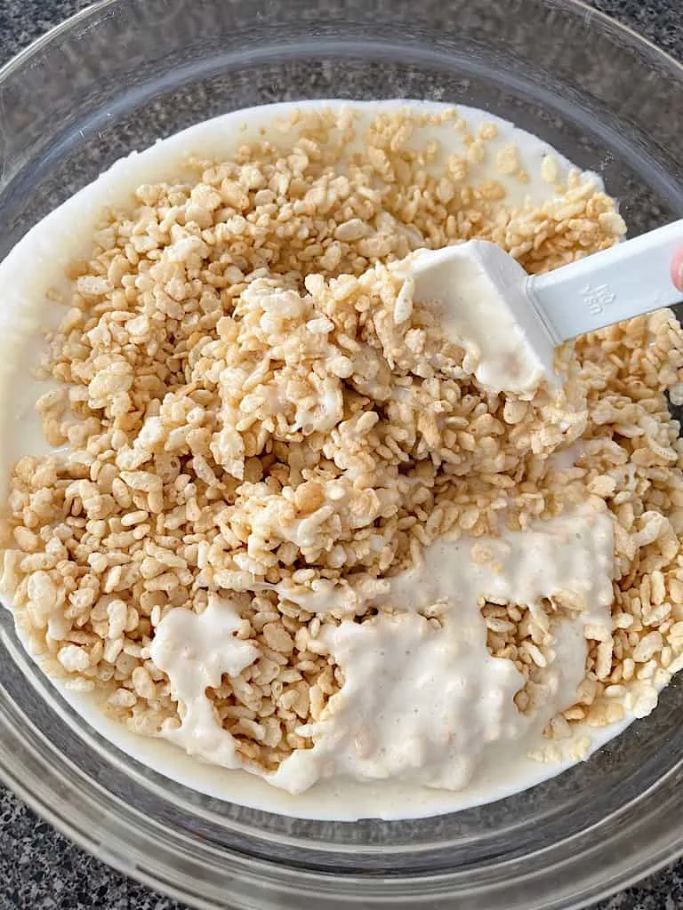 A spoon mixing together melted marshmallows and Rice Krispies cereal.