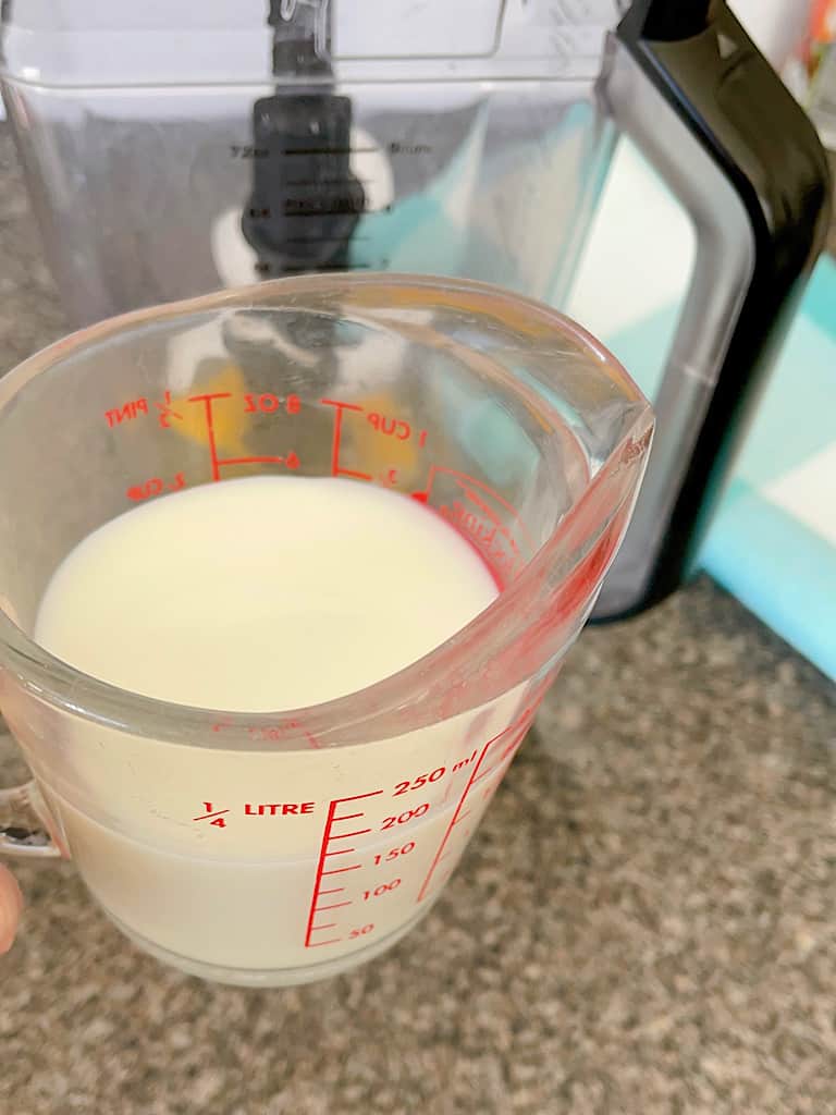 A measuring cup full of milk in front of a blender.