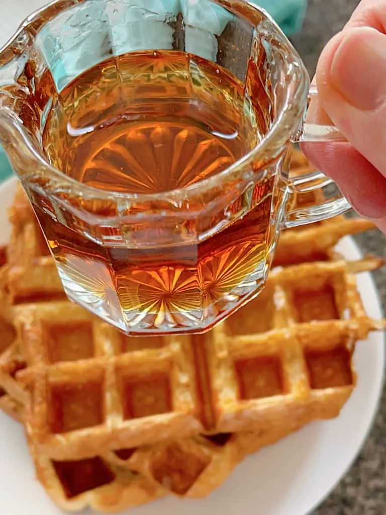 A cup of maple syrup over a stack of French Toast Waffles.