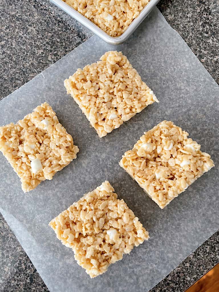 Four Rice Krispie Treat squares on a piece of parchment paper.