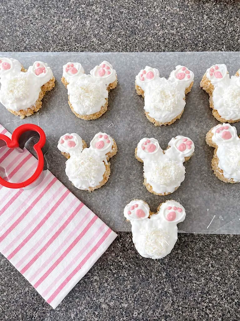 Eight Mickey Bunny Tail Rice Krispie Treats next to a pink and white towel and a Mickey Mouse cookie cutter.