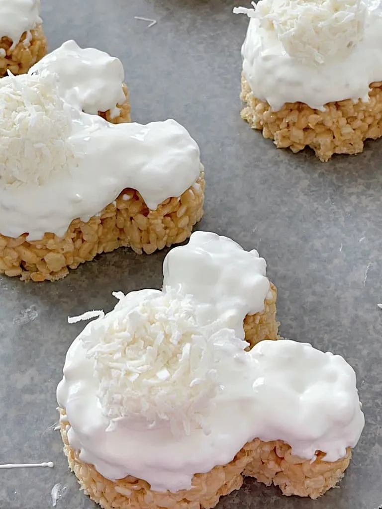 Two Mickey Shaped Rice Krispie treats covered with white candy melts and a marshmallow bunny tail.