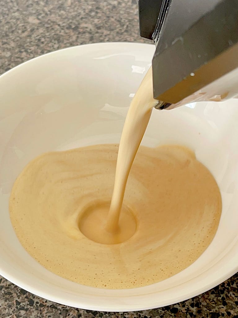 French Toast batter in a blender being poured into a shallow bowl.
