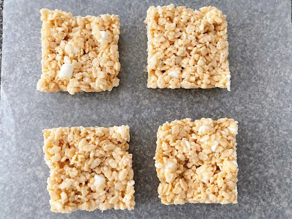 Four Rice Krispies Treats cut into squares on a piece of parchment paper.