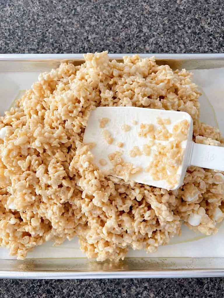 Rice Krispies Treats mixture being spread over a parchment paper-lined baking sheet.