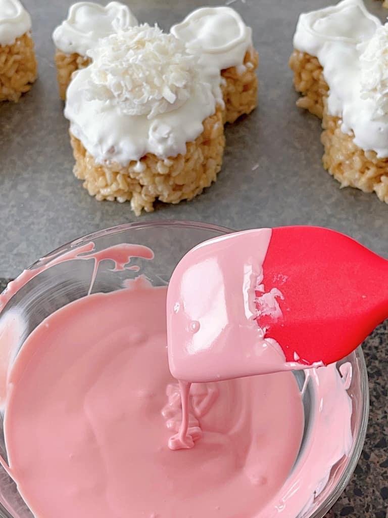 A spatula with a bowl of melted pink candy melts.