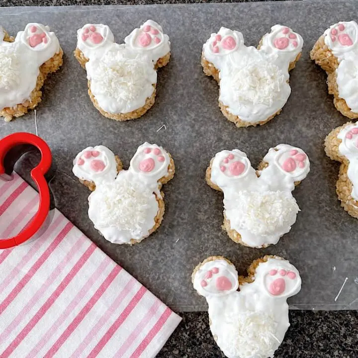 Eight Mickey Bunny Tail Rice Krispie Treats next to a pink and white towel and a Mickey Mouse cookie cutter.