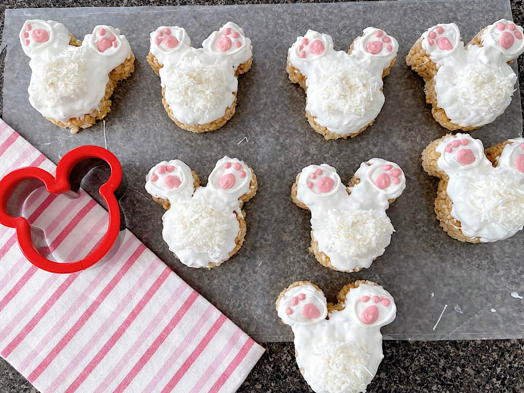 Eight Mickey Bunny Tail Rice Krispie Treats next to a pink and white towel and a Mickey Mouse cookie cutter.