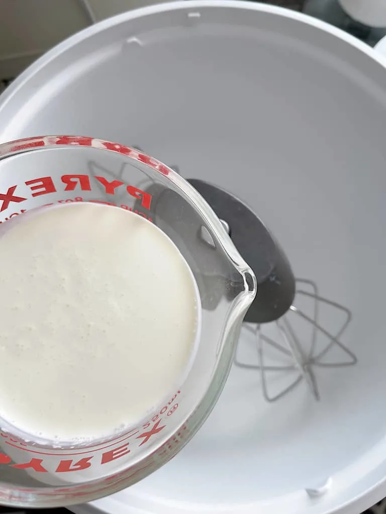 A measuring cup filled with heavy whipping cream over a mixing bowl.