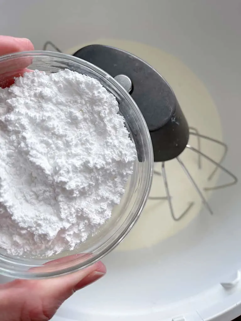 A bowl of powdered sugar over a mixing bowl of heavy cream.