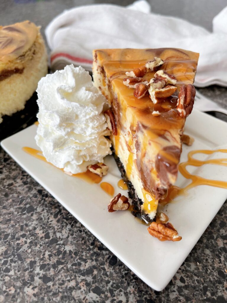 A slice of Cheesecake Factory Caramel Pecan Turtle Cheesecake with whipped cream and caramel sauce.