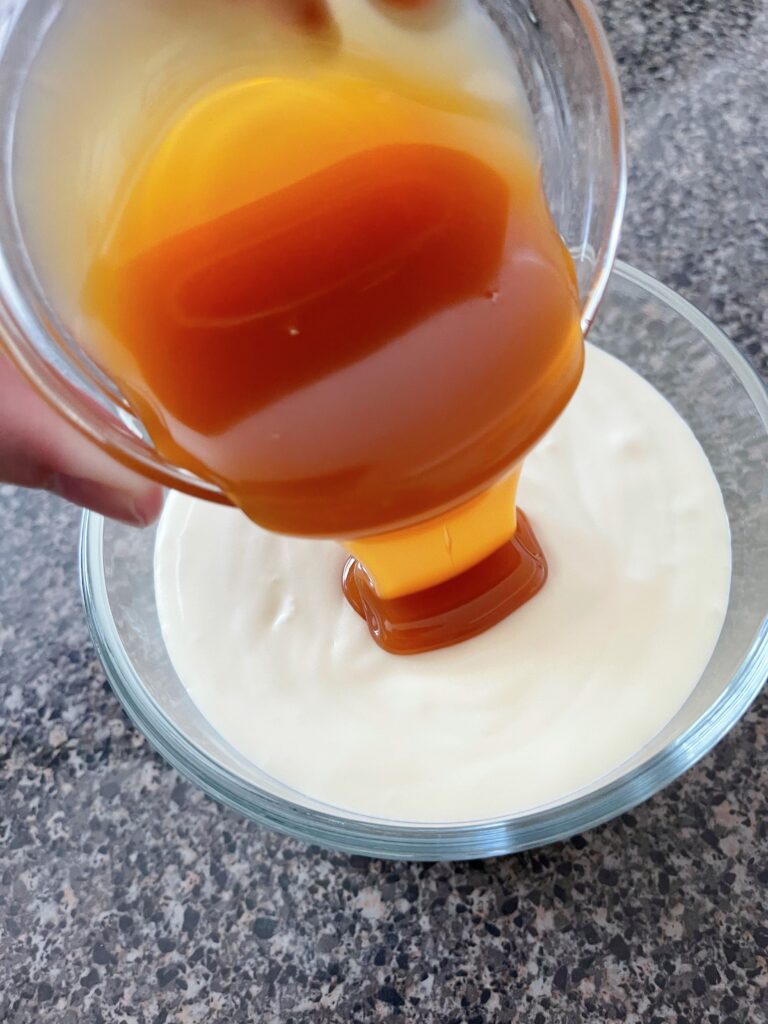 Caramel sauce being poured into a bowl of cheesecake batter.