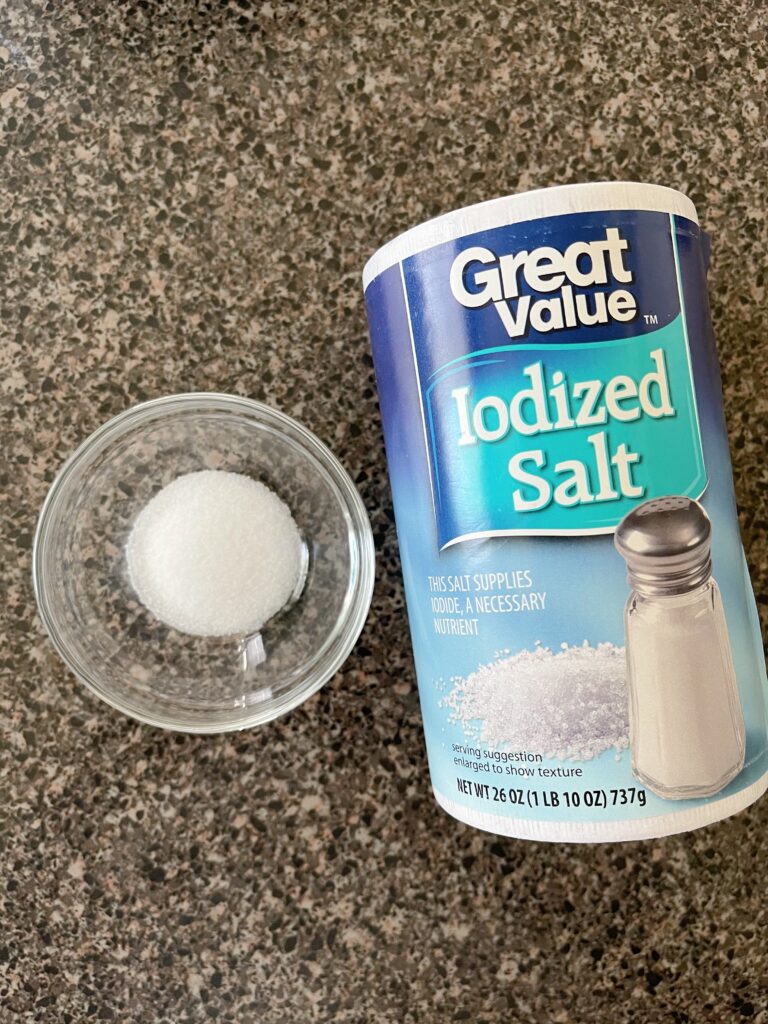 A small bowl of salt next to a cylinder of salt.