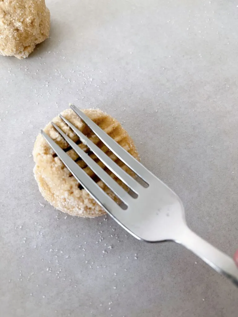 A fork pressing into a peanut butter cookie dough ball.