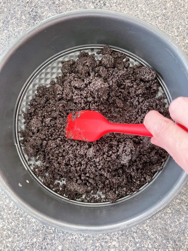 Pressing OREO crust into the bottom of a springform pan.
