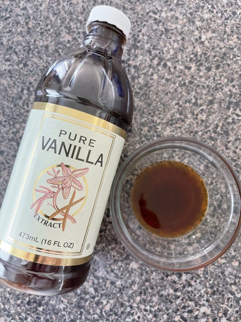 A bowl of vanilla next to a bottle of vanilla.
