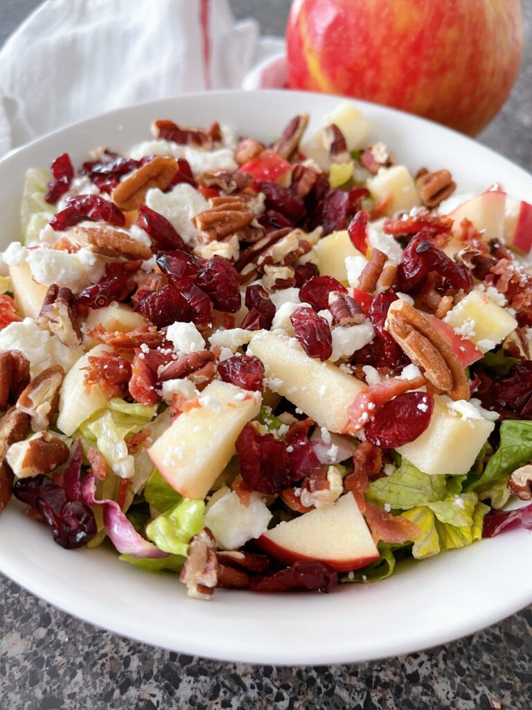 A salad with apples, cranberries, bacon, pecans, and feta cheese.