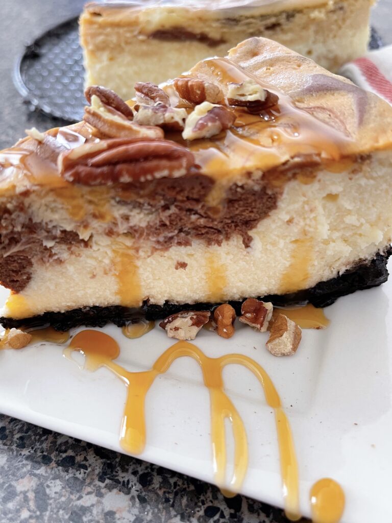 A slice of Cheesecake Factory Caramel Pecan Turtle Cheesecake with whipped cream and caramel sauce.