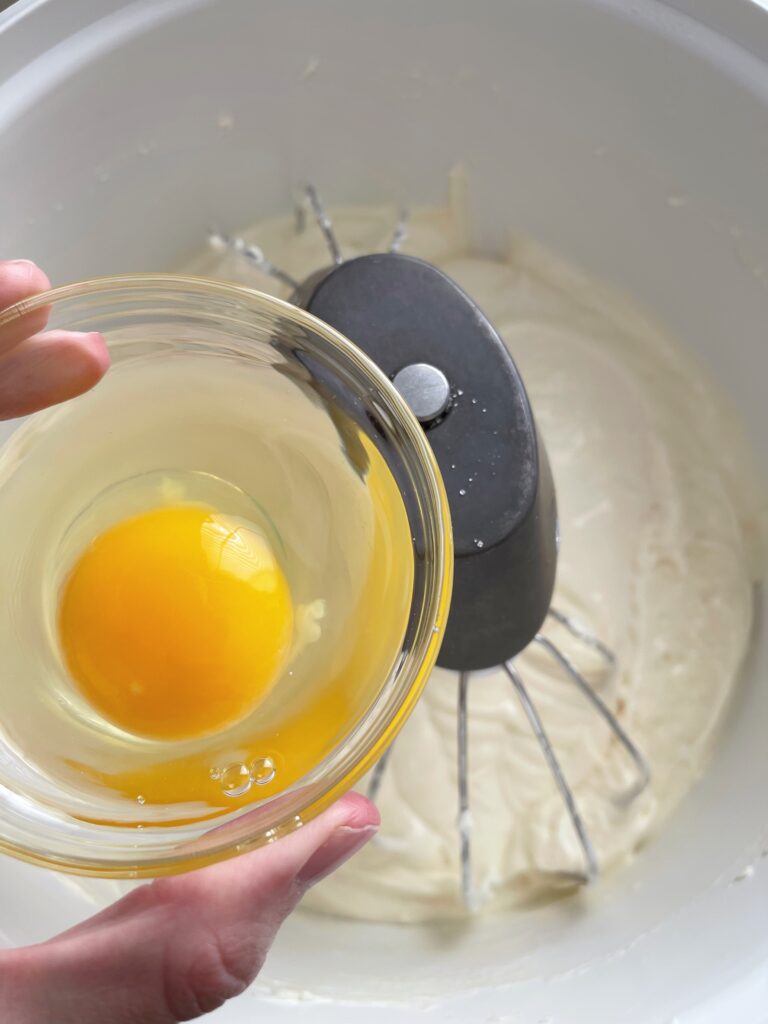 An egg in a bowl over cheesecake batter.