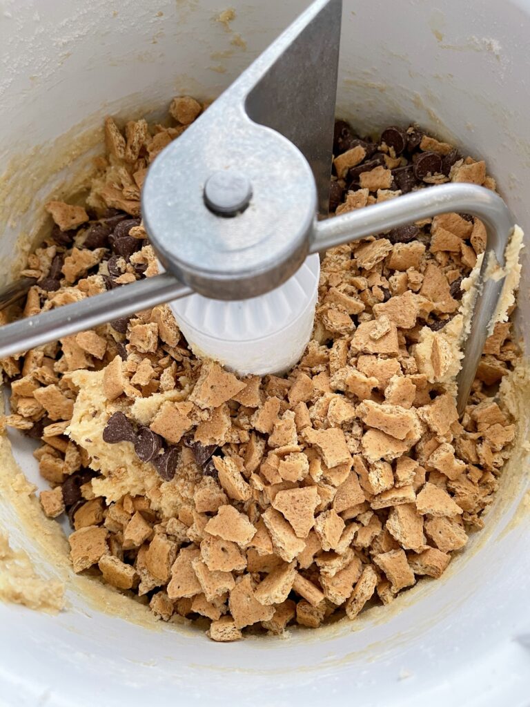 Graham cracker pieces, chocolate chips, and cookie dough in a mixer.