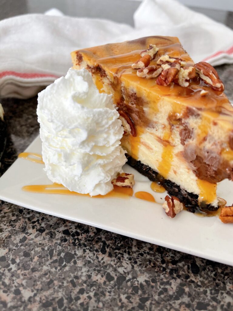 A slice of Cheesecake Factory Caramel Pecan Turtle Cheesecake with whipped cream and caramel sauce.