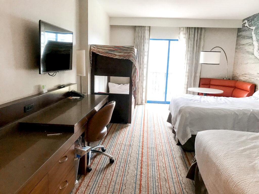 Two queen beds, table, bunk beds, desk, television in a guest room at Courtyard Anaheim Theme Park Entrance.