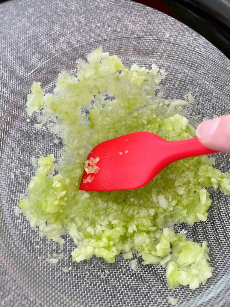 A spatula smashing diced cucumbers to remove liquid for tzatziki sauce.