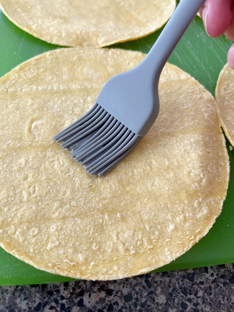 A brush applying oil to the top of a corn tortilla.