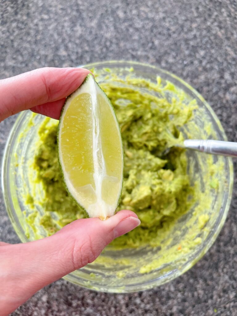 A lime wedge and a bowl of smashed avocados.