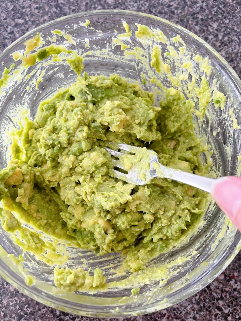 A fork smashing avocados in a bowl.