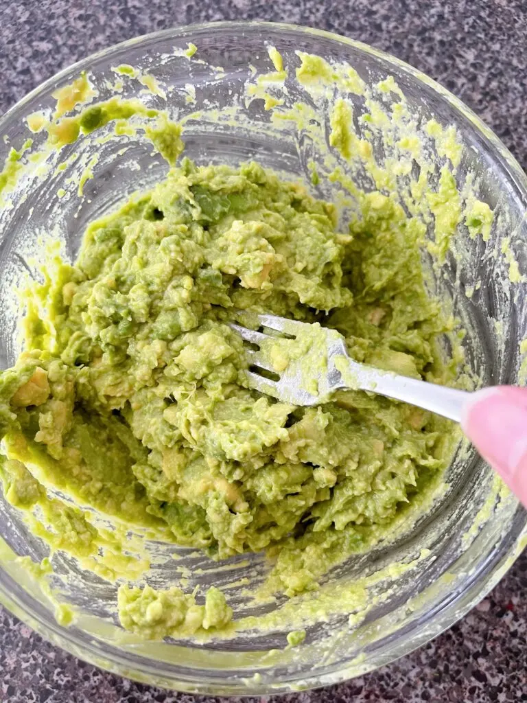 A fork smashing avocados in a bowl.