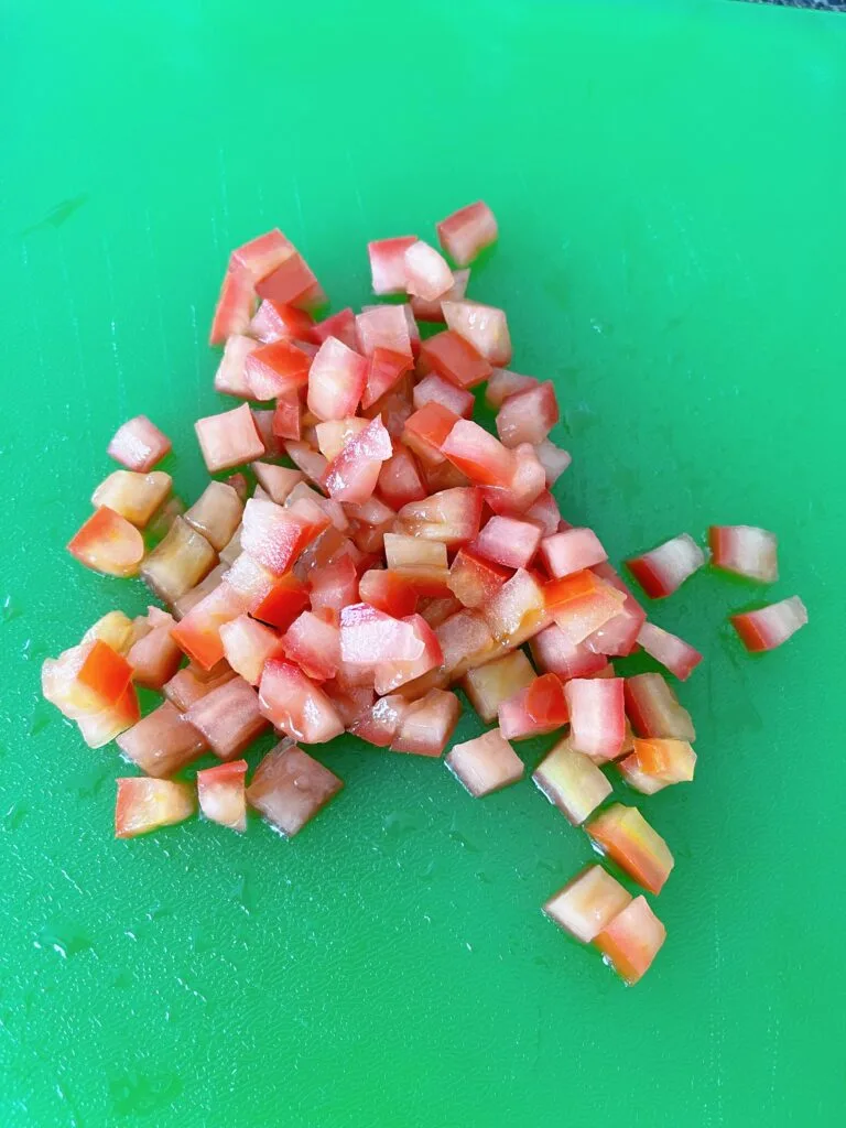 Chopped roma tomatoes on a green cutting board.