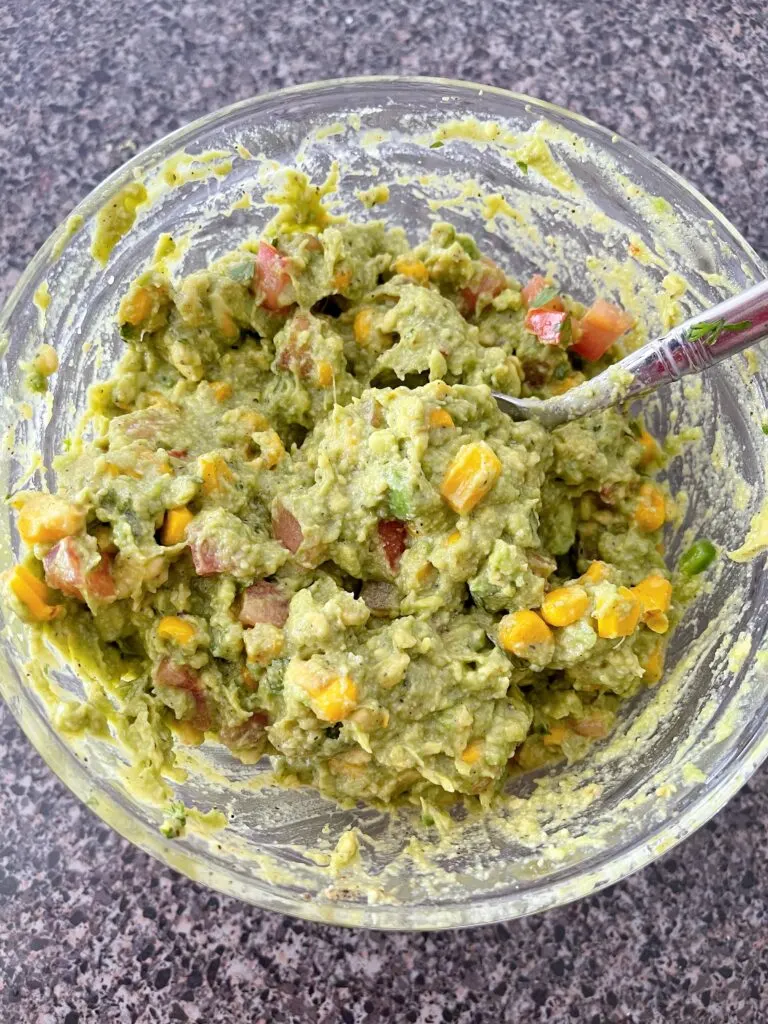 A bowl of chunky guacamole with diced tomatoes and roasted corn.