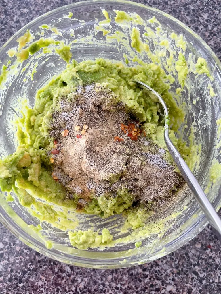 Spices in a bowl of smashed avocados.