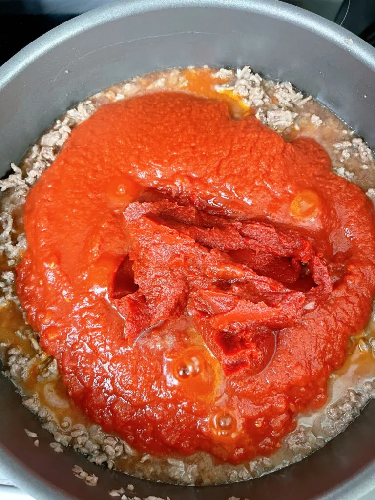 Tomato sauce, crushed tomatoes, tomato paste and ground beef in a pan.