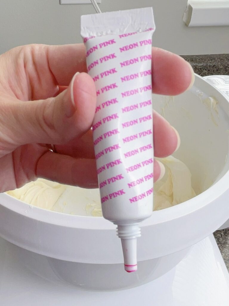 Pink food coloring over a bowl of frosting.