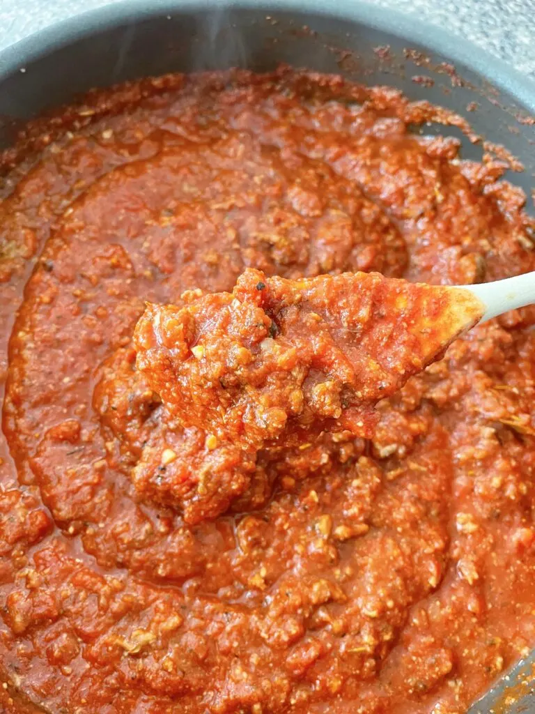 Spaghetti sauce in a pan with a wooden spoon.