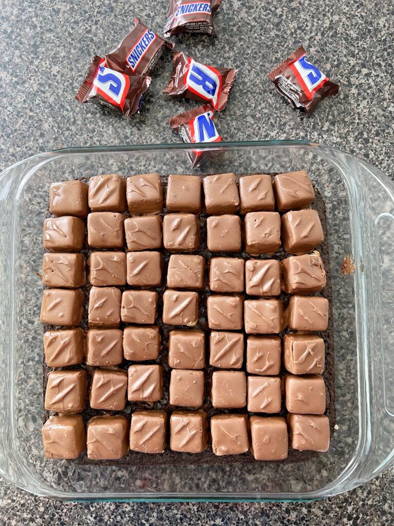 Unwrapped Snickers Mini candy bars on a pan of brownies.