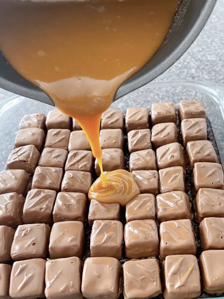 Melted caramel being poured over Snickers and brownies.