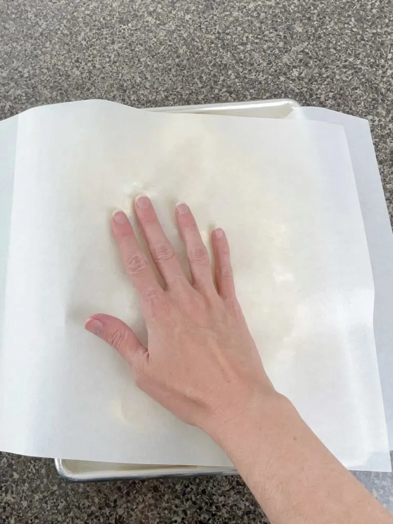 A hand pressing cookie dough on a baking sheet to level it.