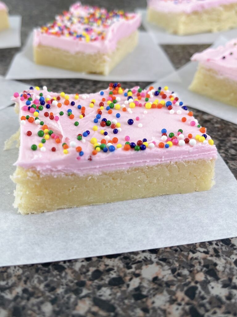 A cream cheese sugar cookie bar with pink frosting and sprinkles.