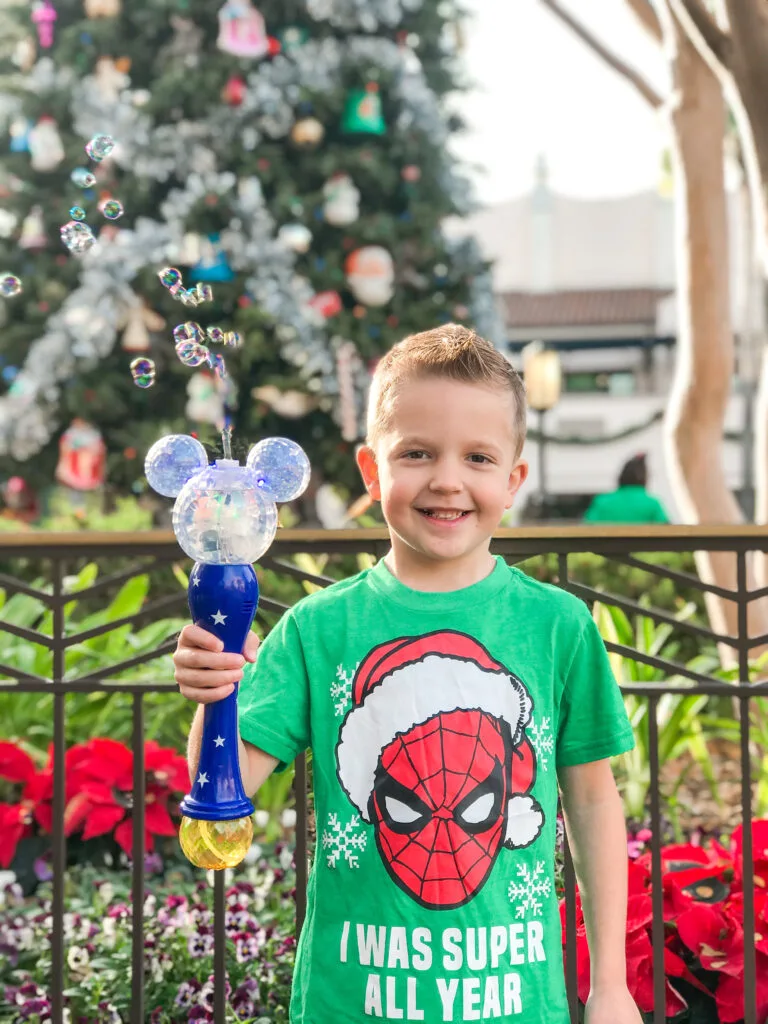 A boy in a Spider-Man Christmas shirt with a Mickey Mouse bubble wand.