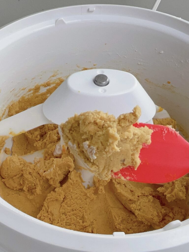 Pumpkin sugar cookie dough on a spatula over a stand mixer bowl.