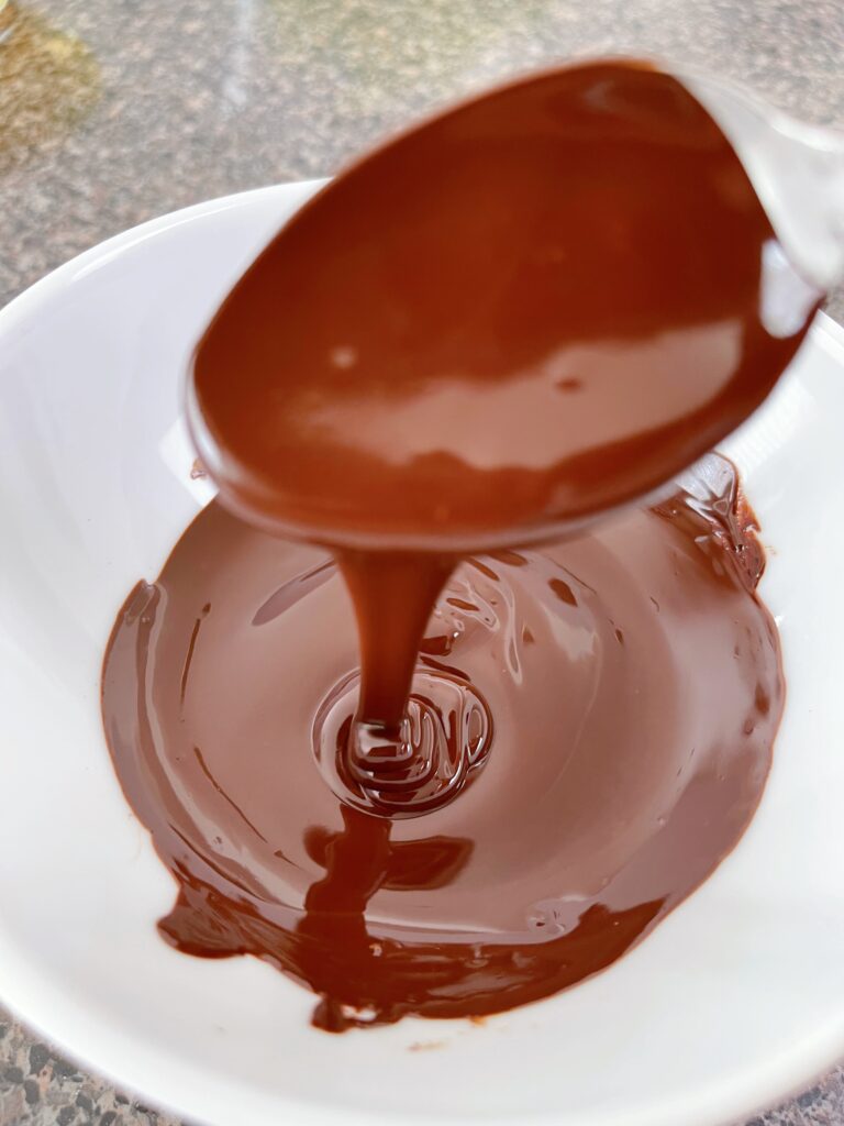 A bowl and spoon of melted chocolate.