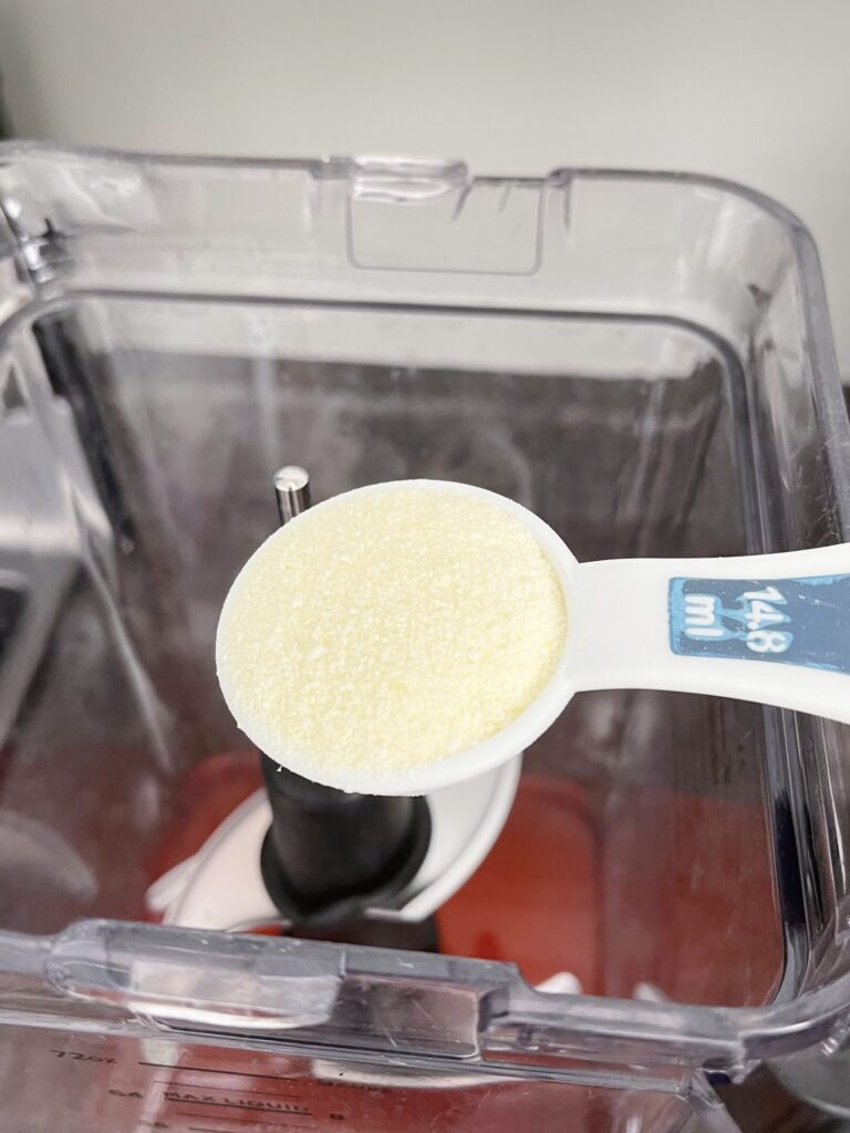 A tablespoon full of lemonade drink mix over a blender.